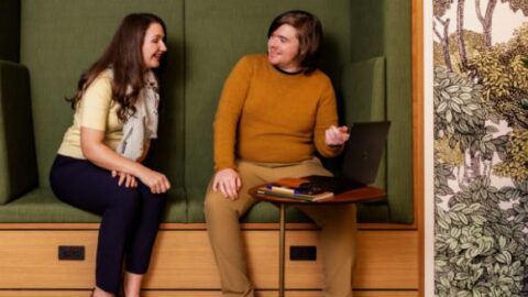 An image of two people on a bench referencing a laptop on a small desk nearby.